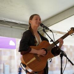 Ella Belfanti playing guitar and smiling at camera.