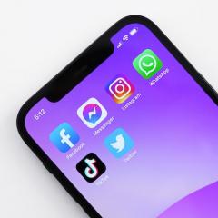 Iphone with purple wallpaper and a variety of social media apps on a page