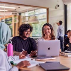 Two students sitting at a desk smiling at content on a laptop.
