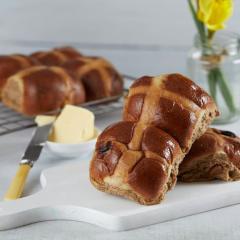 Hot cross buns on a white kitchen table top with a chunk of butter sitting in a small bowl