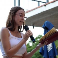 Female student holding a microphone and reading poetry from a book