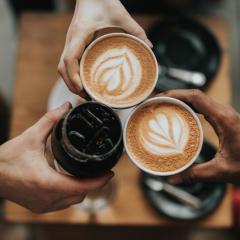 Three people holding cups of coffee together as they "cheers" each other