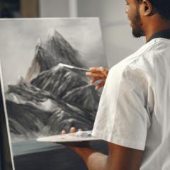 Young man holding a paintbrush and painting a snowy mountain on a canvas