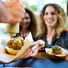 Food truck vendor squeezing sauce onto meatballs as customers wait with smiles.