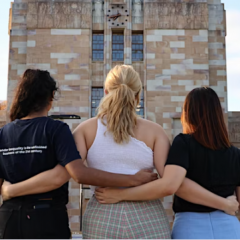 Three women standing with their backs to us facing the Forgan Smith building, arm in arm