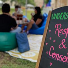 "Respect" hand written on a chalkboard with a group of students sitting on bean bags in the background talking